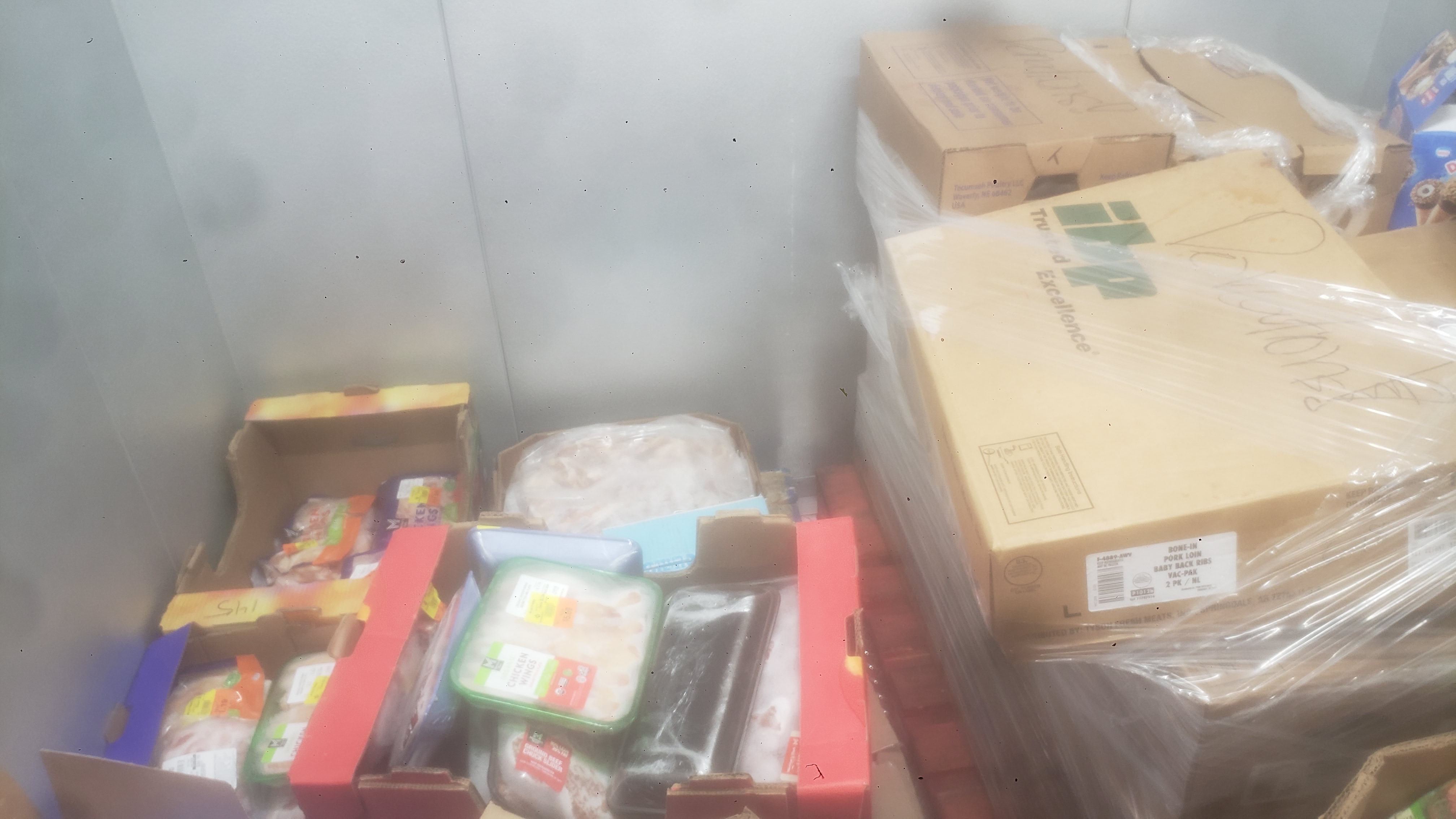 Assorted frozen items in cardboard boxes and trays such as chicken wings, chicken thighs, and pork.